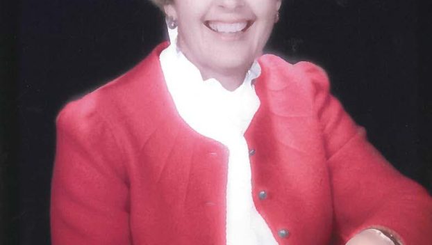 An older white woman wearing a red jacket and a white blouse smiles for a portrait.