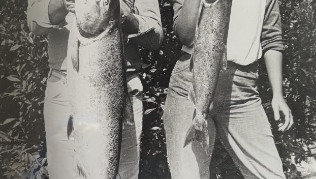 Conrad Mann, left, holds a large fish proudly in a black-and-white photo, smiling proudly. Standing next to him is his daughter, also holding a fish and smiling proudly.