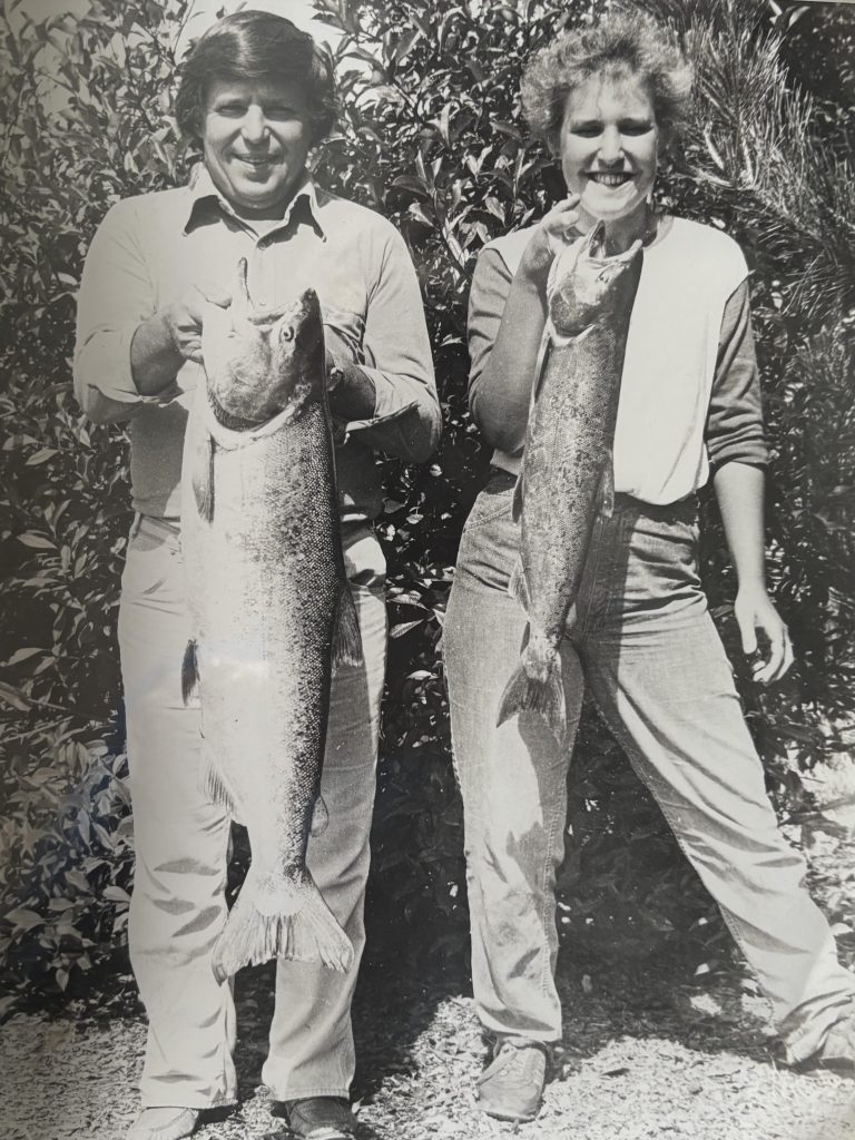 Conrad Mann, left, holds a large fish proudly in a black-and-white photo, smiling proudly. Standing next to him is his daughter, also holding a fish and smiling proudly.