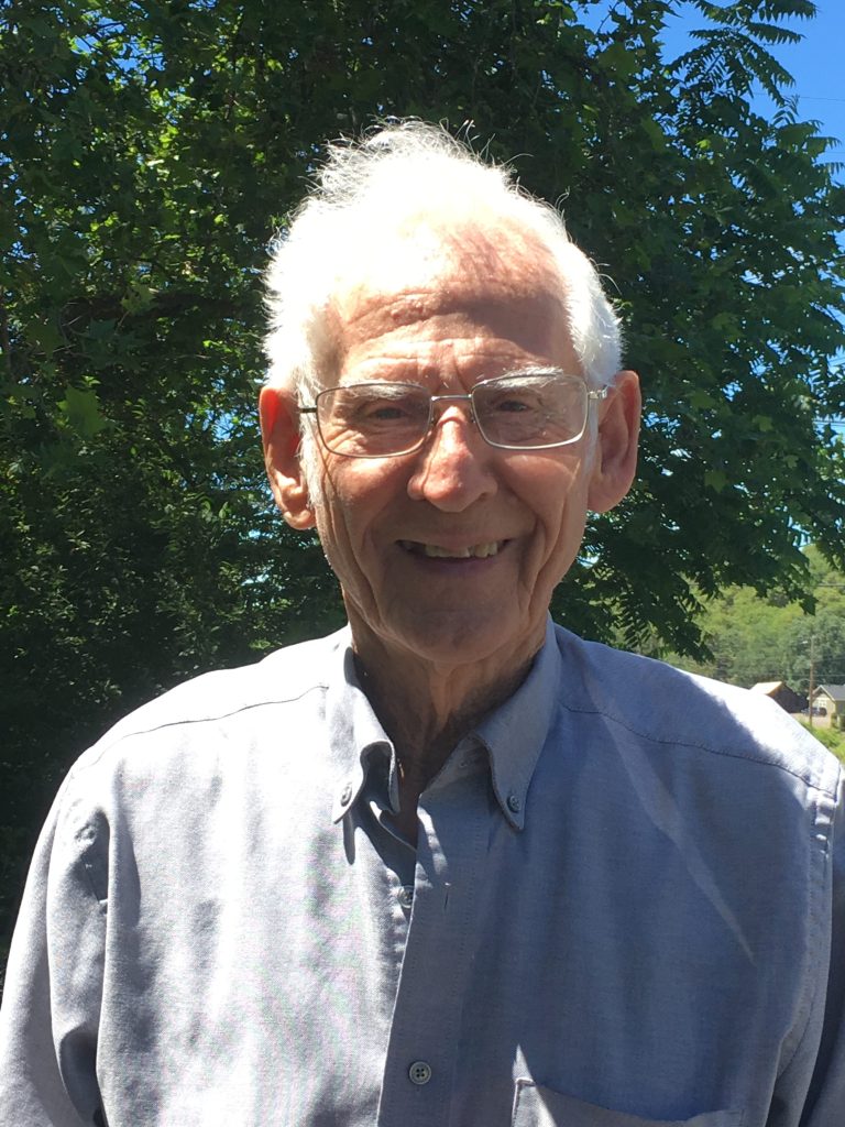 A smiling older white man poses for the camera, looking good-humored on a sunny day.