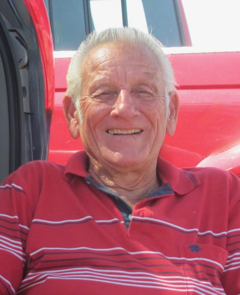 An older white man with close cropped white hair in a red shirt is seated, smiling at the camera. He looks easygoing and kind.
