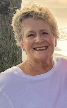 An older white lady with short white hair wearing a white t-shirt is smiling for the camera. She looks very happy.