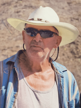 A rugged looking white man with a cowboy hat and wraparound sunglasses